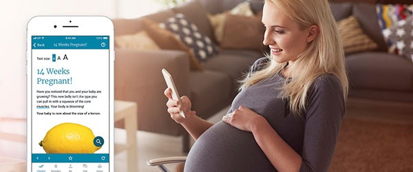 Expectant mother gently touching her baby bump and using a mobile phone.