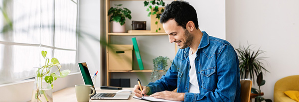 Man writing at desk with laptop