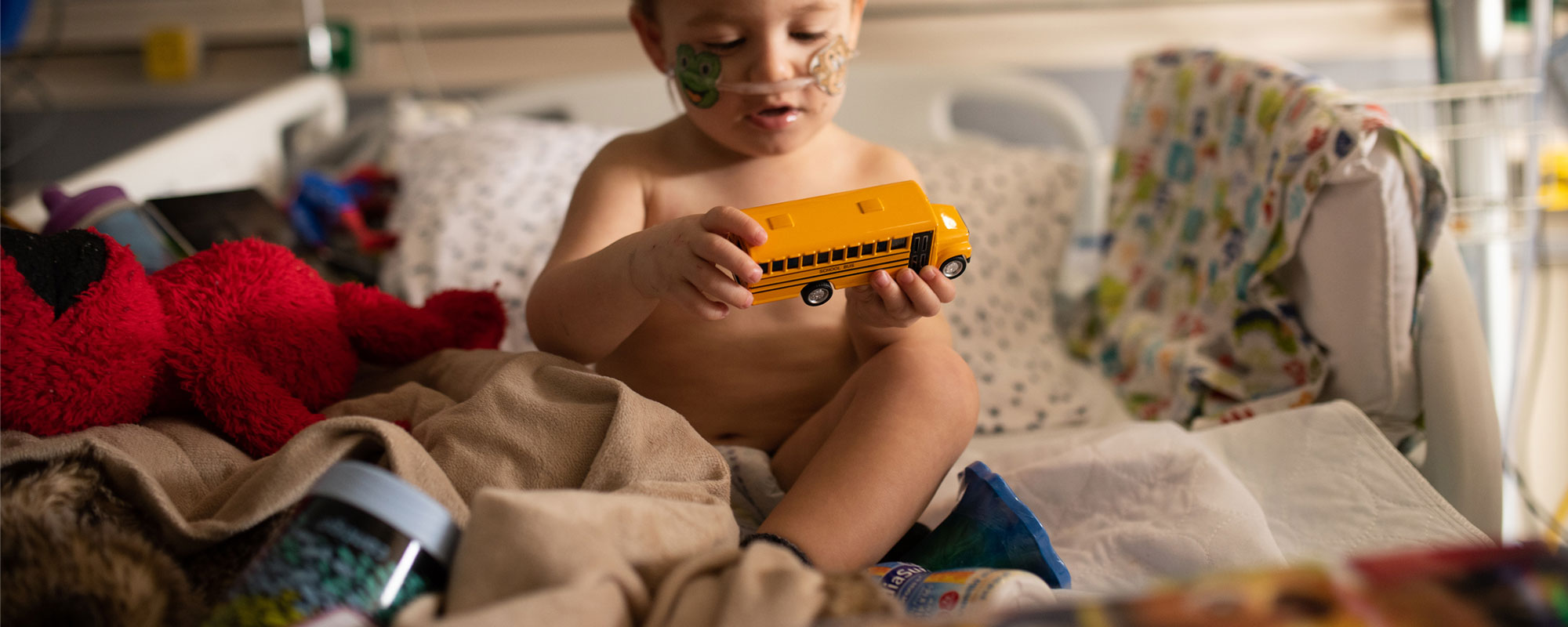 Toddler recovers in hospital pediatric intensive care unit and plays with a toy yellow bus