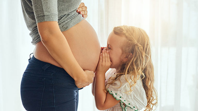 Toddler whispering to mom's pregnant belly.