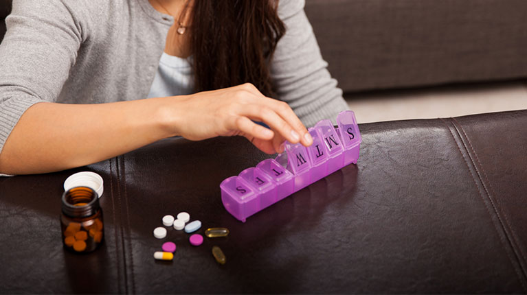 Woman putting her vitamins and daily pills into a pill box.