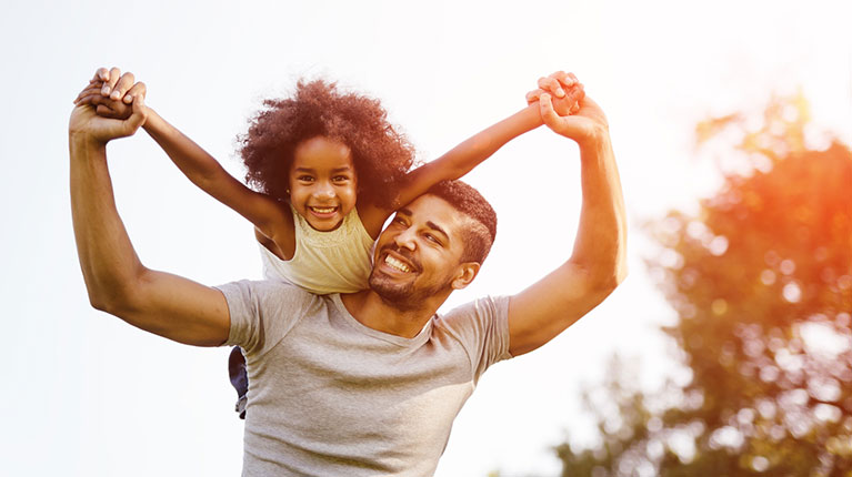 Father holding up his daughter in a park.