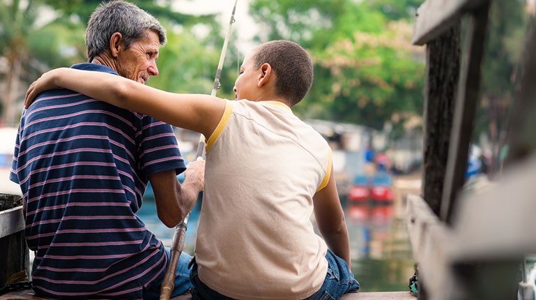 Old man and boy fishing together on river for fun.