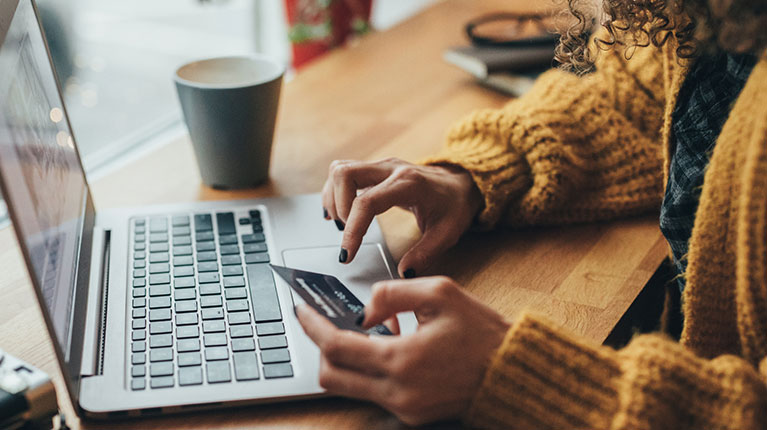 Woman with curly hair, paying her bill online while drinking a coffee.