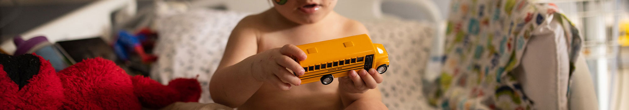 Toddler recovers in hospital pediatric intensive care unit and plays with a toy yellow bus