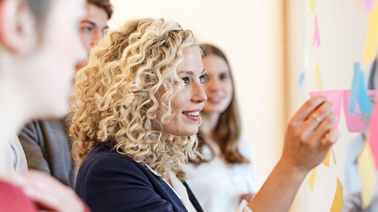Woman putting post-it notes on a white board.