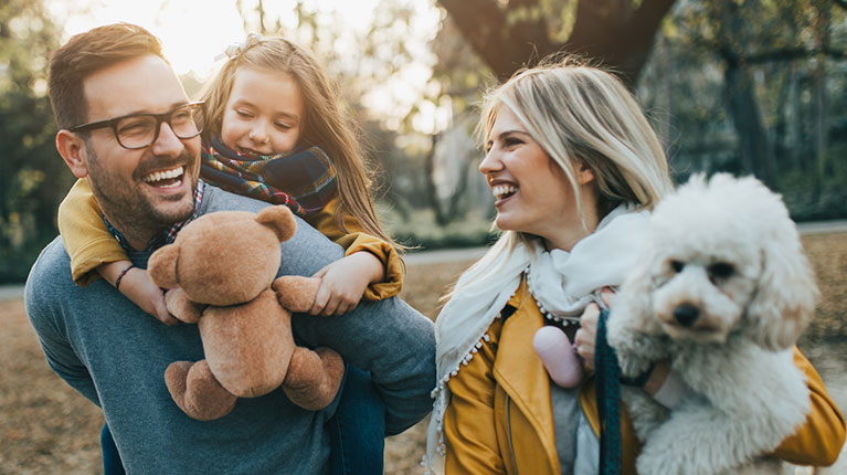 Parents and daughter walking outside in the fall with their dog.