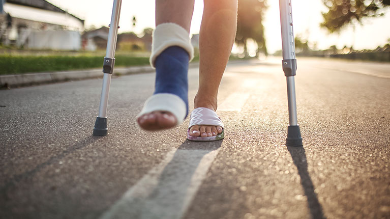 Woman with broken leg on crutches walking down the street.
